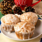 Three Spiced Eggnog Muffins with white glaze and cinnamon topping on a white plate, surrounded by holiday decorations