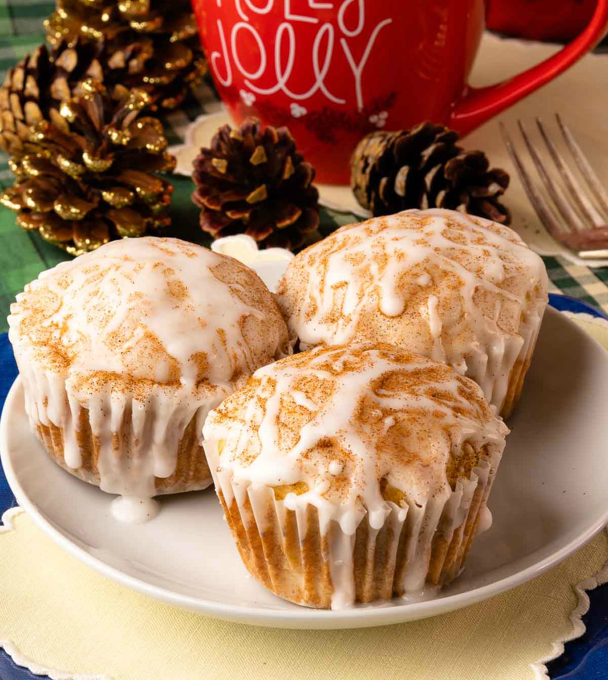 Three Spiced Eggnog Muffins with white glaze and cinnamon topping on a white plate, surrounded by holiday decorations