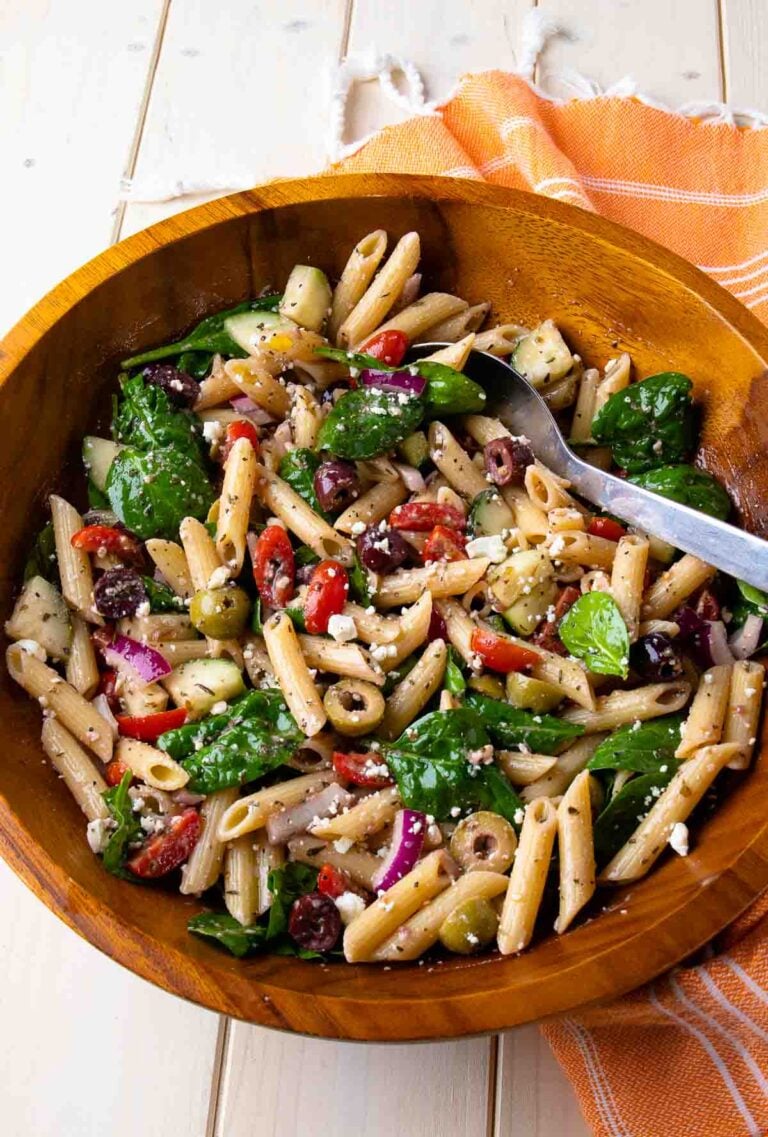 Mediterranean Pasta Salad with penne, spinach, olives, red peppers, and feta in wooden bowl with serving spoon