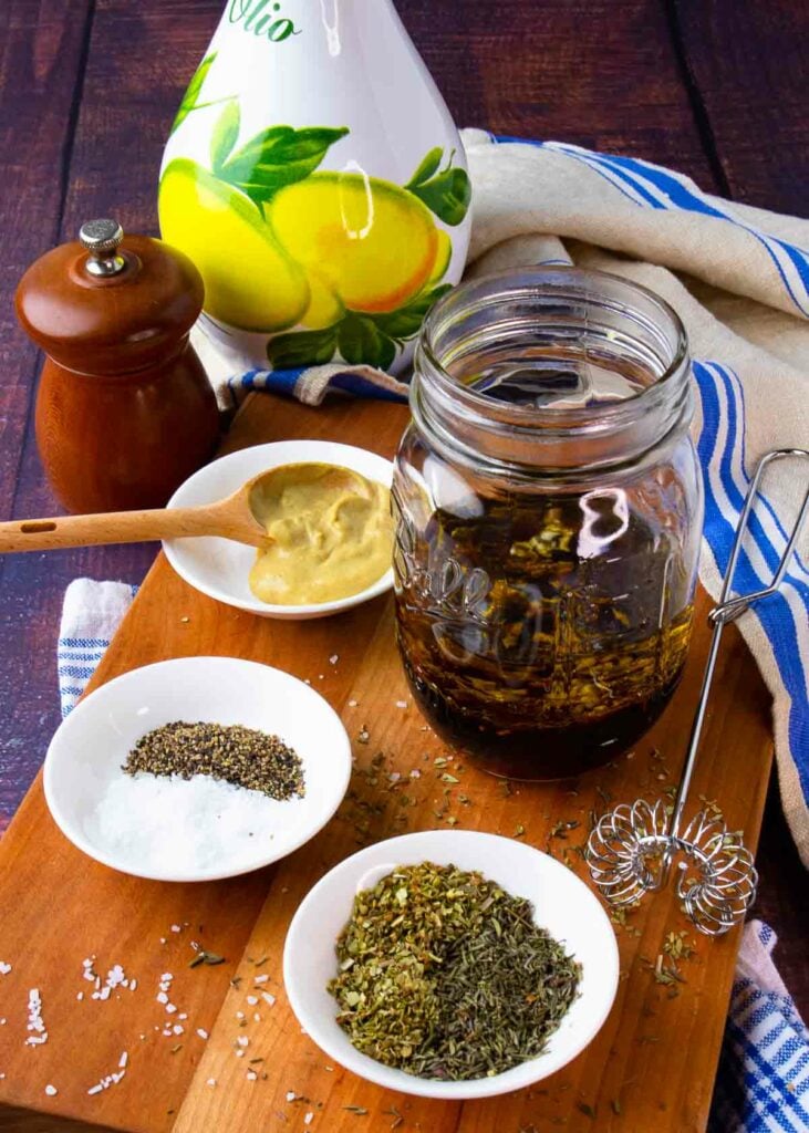 Greek salad dressing ingredients with olive oil and red wine vinegar in a jar with whisk.