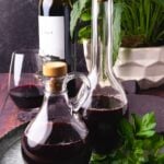 Two glass bottles of homemade red wine vinegar on a metal tray with greenery.