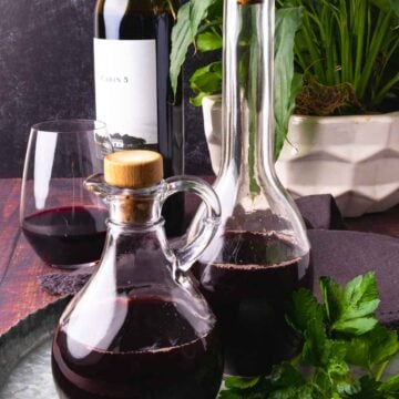 Two glass bottles of homemade red wine vinegar on a metal tray with greenery.