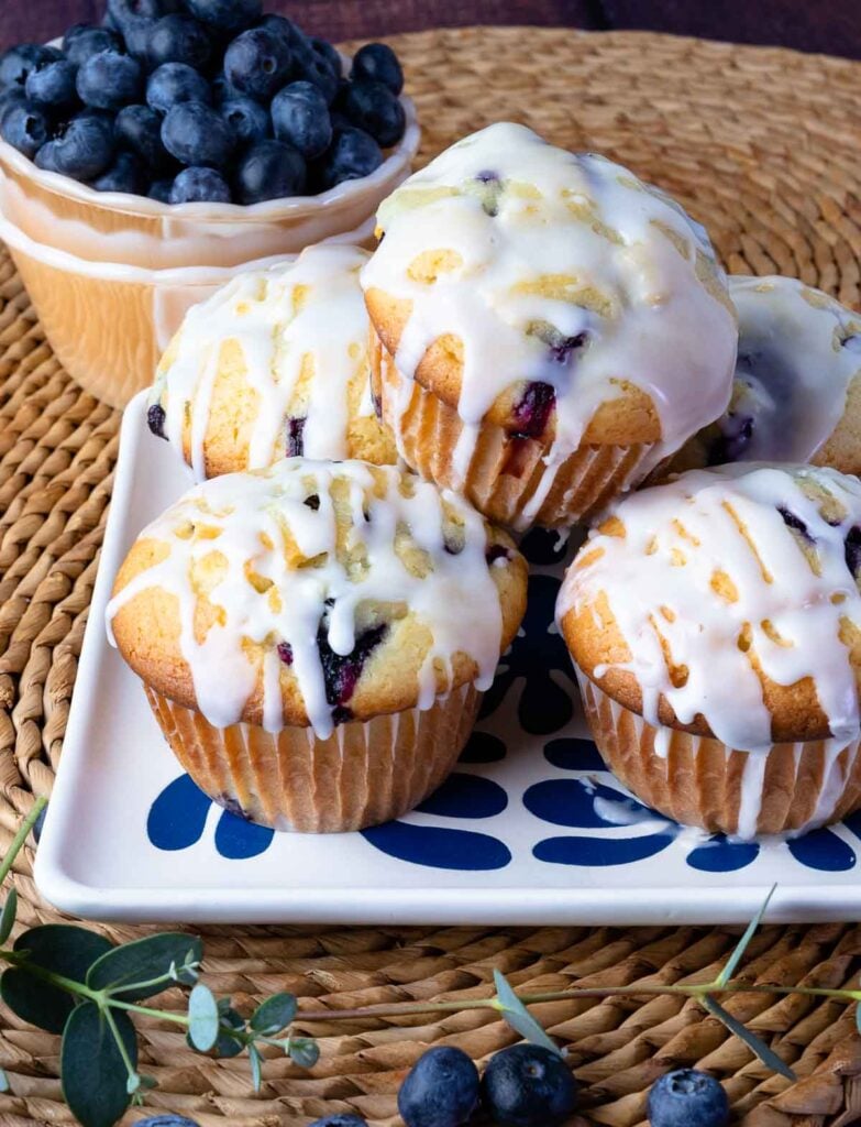 Blueberry Sour Cream Muffins with Lemon Glaze stacked on a blue and white plate.