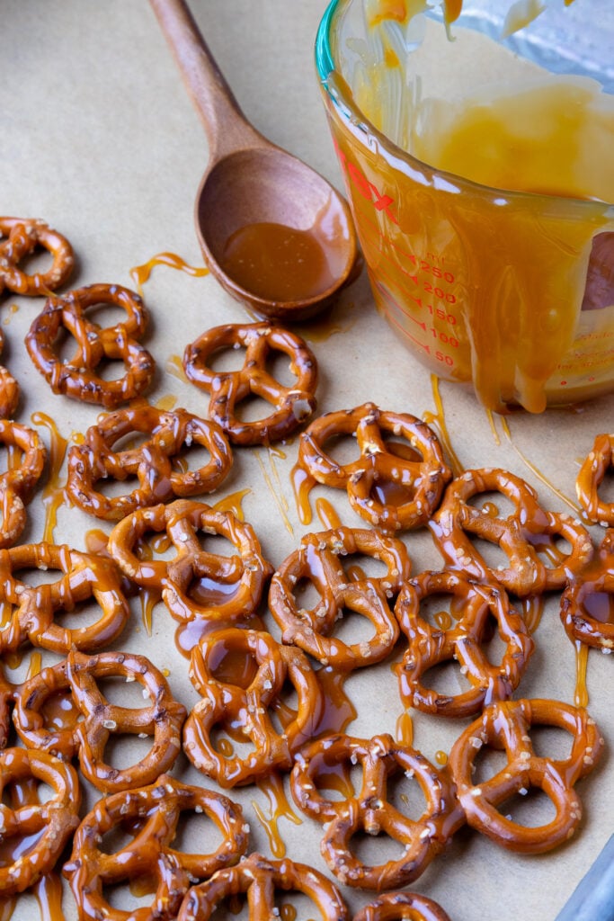 These crunchy pretzels are laid out on parchment paper, drizzled with a buttery caramel sauce, waiting to be covered in rich melted chocolate.