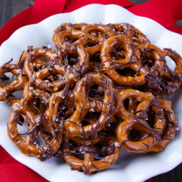 Chocolate Caramel Pretzels with Sea Salt on a white plate with red ribbon decorations.