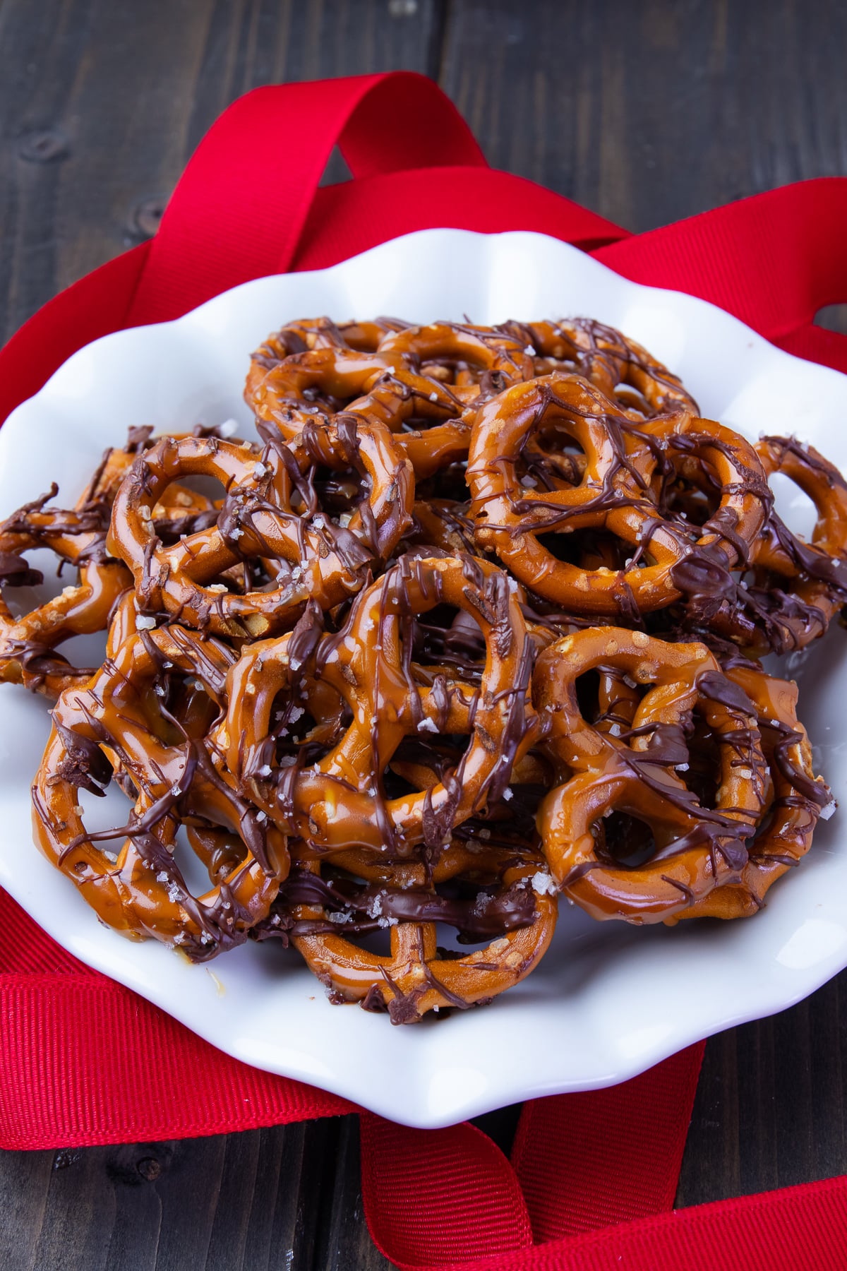 Chocolate Caramel Pretzels with Sea Salt on a white plate with red ribbon decorations.