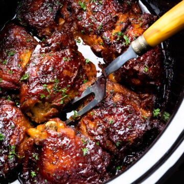 Crock Pot Chicken Thighs in bowl of pot with serving fork.