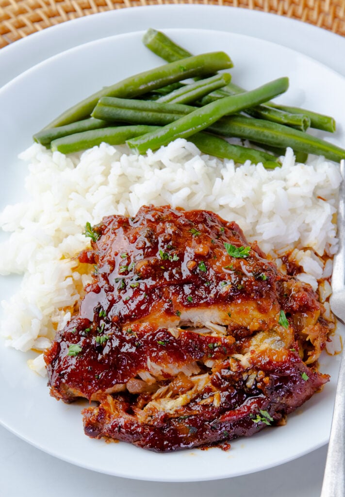 Sliced Crock Pot Chicken Thigh with rice and green beans on a white plate.
