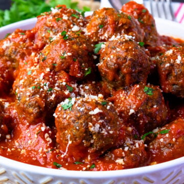 Homemade meatballs in tomato sauce in a white bowl with parsley on top.