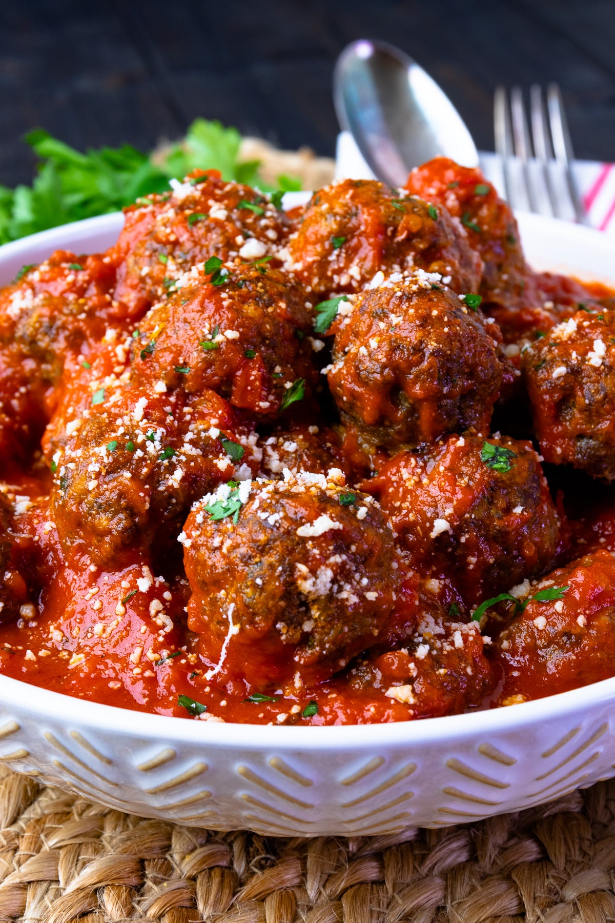 Homemade meatballs in tomato sauce in a white bowl with parsley on top.