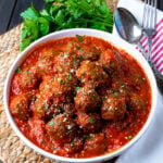 Homemade Meatballs in a white bowle with a napkin, spoon and fork.