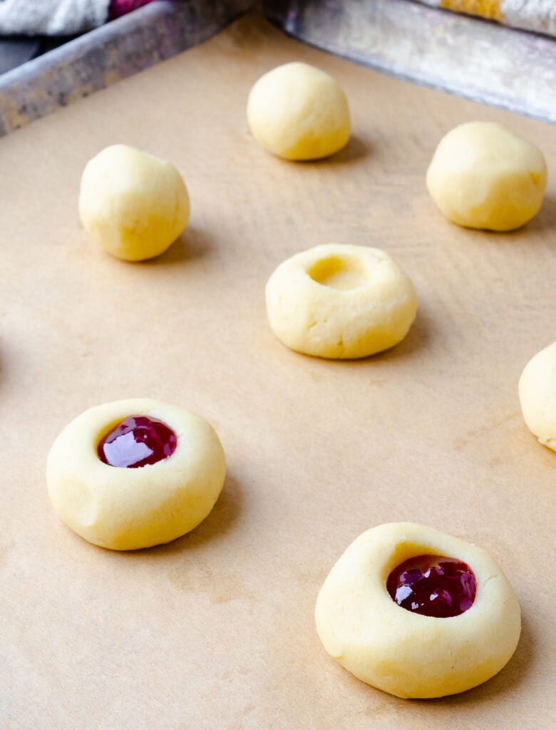 Thumbprint cookie dough in balls on a parchment lined baking sheet.