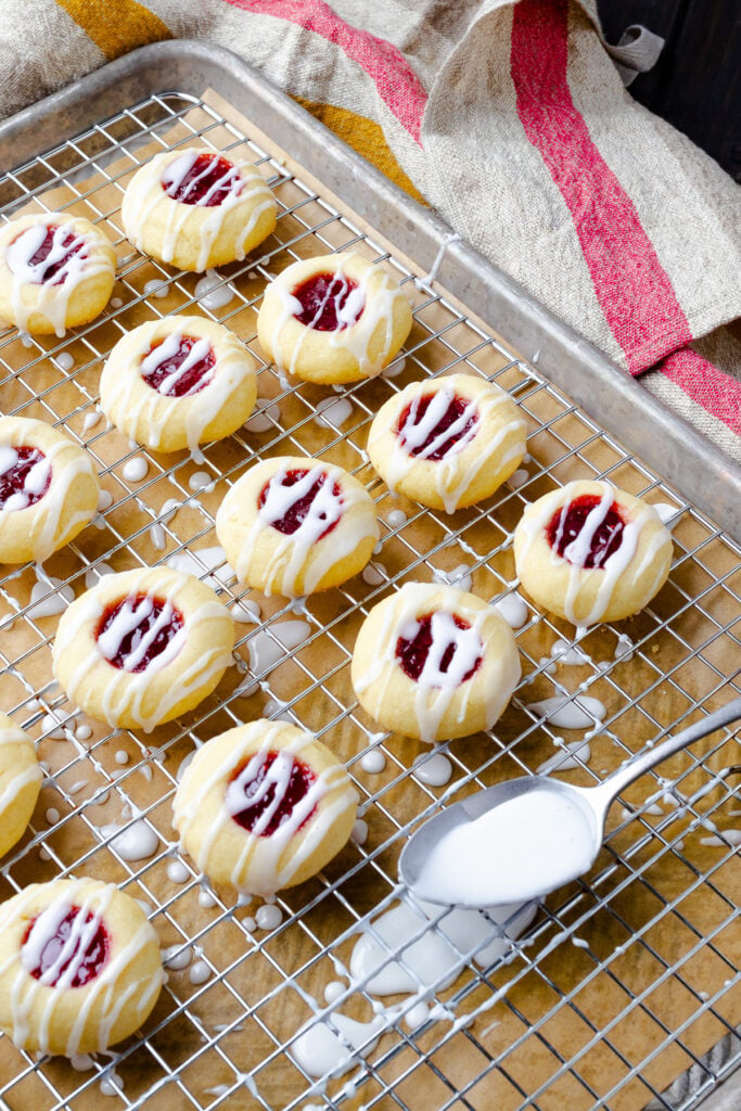 Jam Thumbprint Cookies on a cooling rack drizzled with glaze from a spoon.