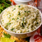 Instant Pot Coconut Lime Rice in white bowl garnished with fresh cilantro and lime wedges, served with forks