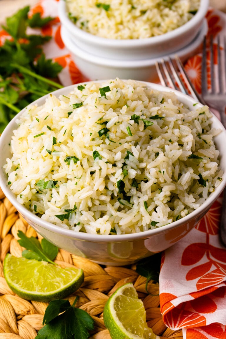 Instant Pot Coconut Lime Rice in white bowl garnished with fresh cilantro and lime wedges, served with forks