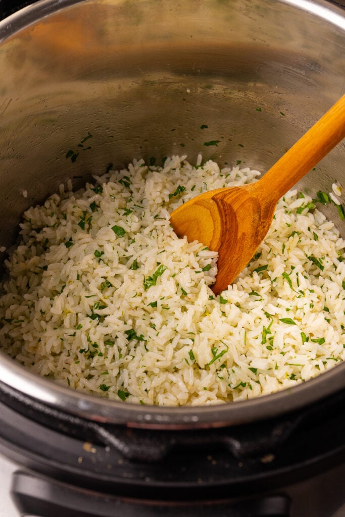 Instant Pot with wooden spoon and coconut lime rice with parsley.