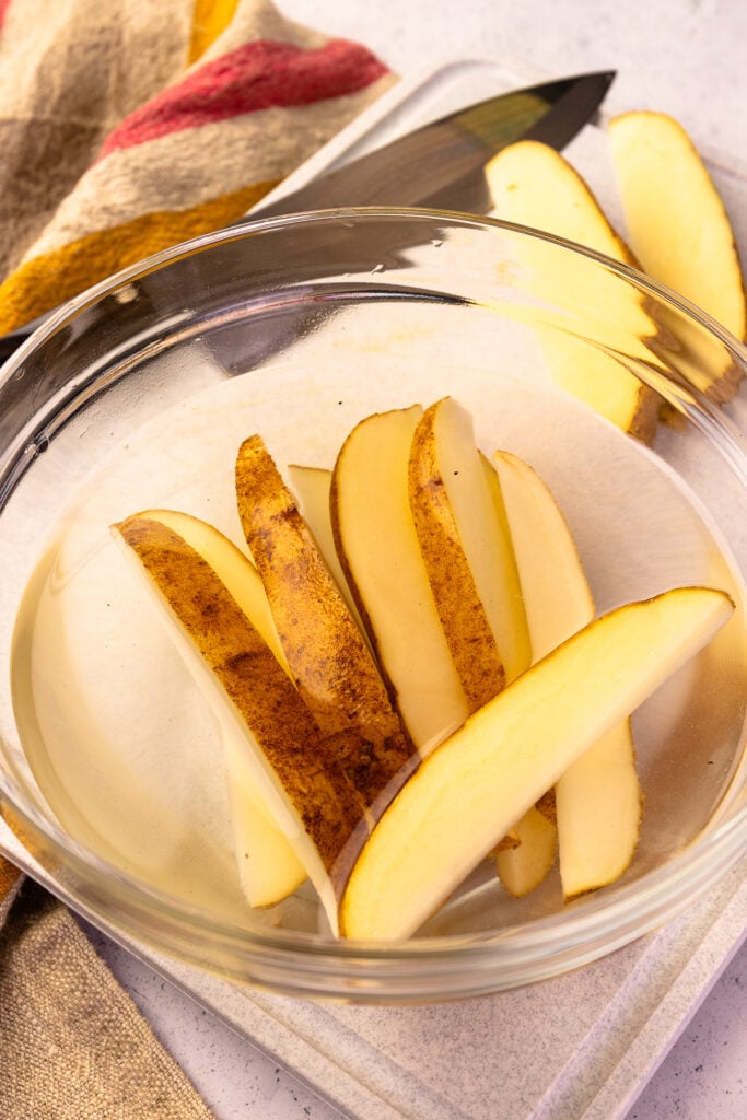 Potato wedges soaking in water before cooking in the air fryer.