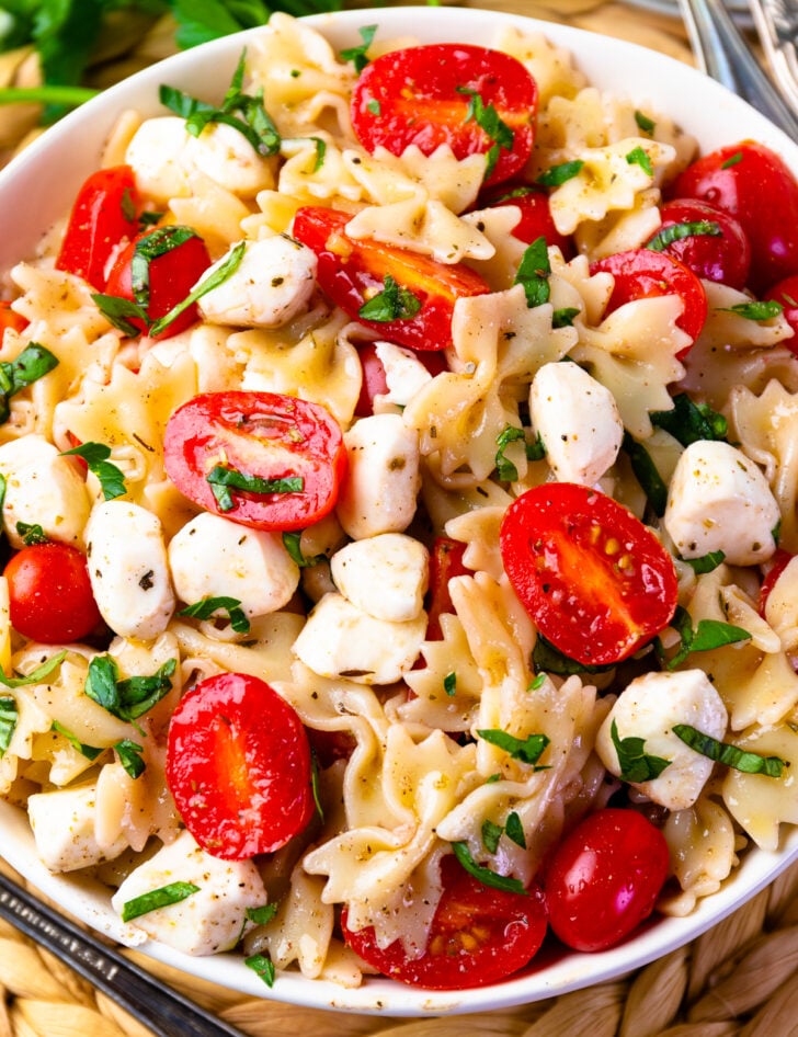 Caprese pasta salad in white bowl with farfalle pasta, fresh mozzarella, cherry tomatoes, and basil garnish on wooden surface
