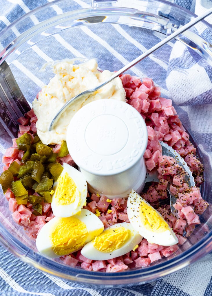 Ham Salad with eggs, pickles, pepper and mayonnaise in a food processor bowl.