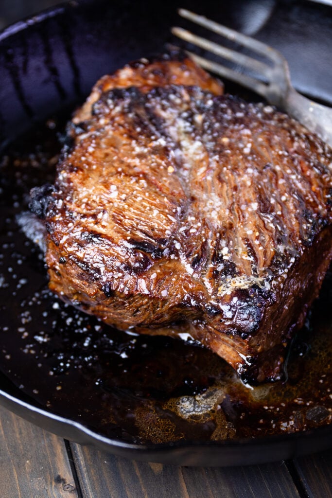 Marinated London Broil in a cast iron skillet with a fork.