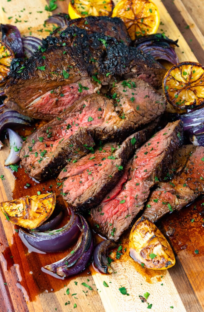 Marinated London Broil on a cutting board with seared lemons and onions.