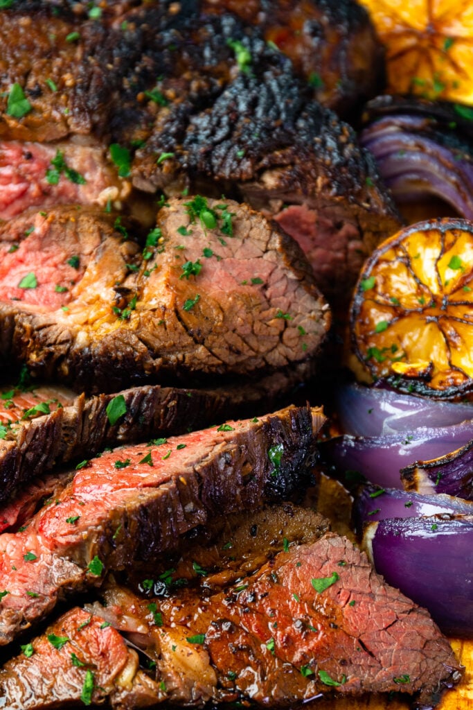 Close up of marinated london broil with seared lemons and onions.
