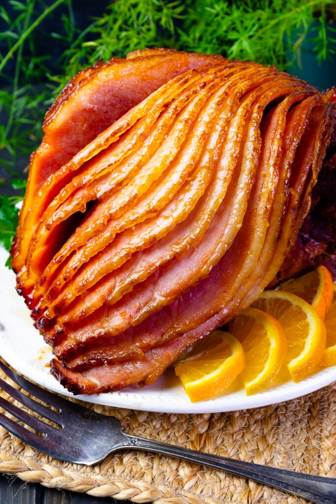 Orange and Pepper Jelly Glazed ham on a platter with fresh oranges for the holiday meal.