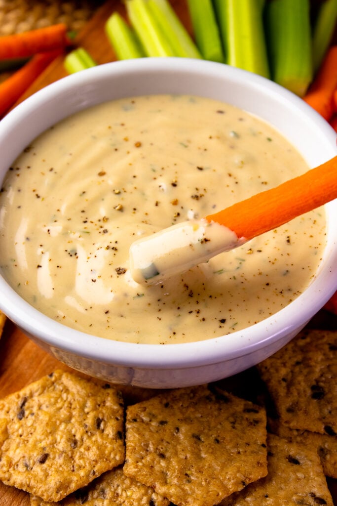 White bowl with Garlic Herb Tahini Dressing and Dip with a carrot.