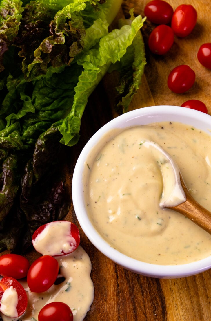 Spoon in a bowl of Garlic Herb Tahini Dressing and Dip with lettuce and tomatoes