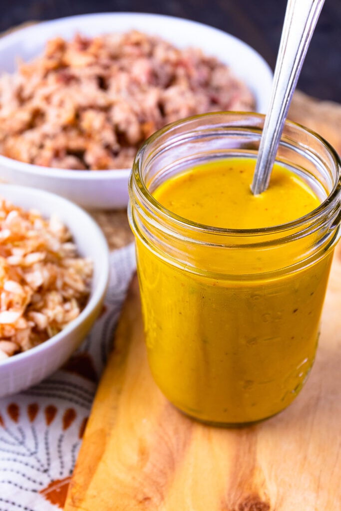 Carolina Gold BBQ Sauce in a mason jar with a spoon for drizzling.