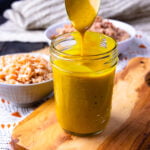 Carolina Gold BBQ Sauce dripping off a spoon to be served with pulled pork and red slaw.