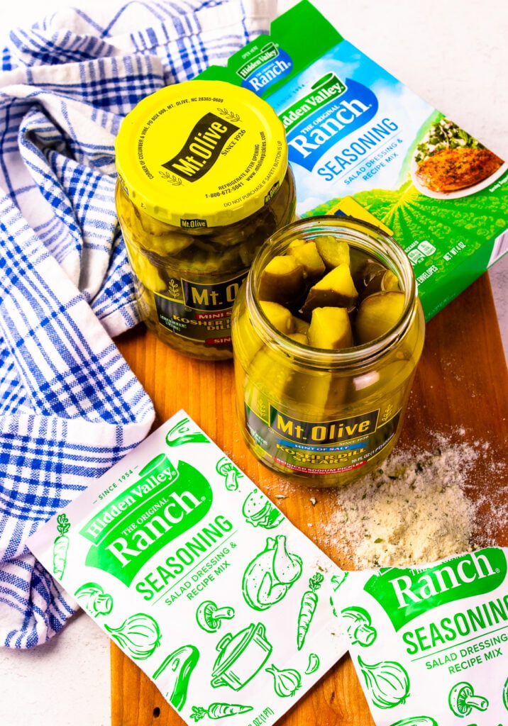 An open jar of Mt. Olive pickles with a packet of Ranch seasoning mix partially visible, showing the powdery seasoning sprinkled on top of the pickles.