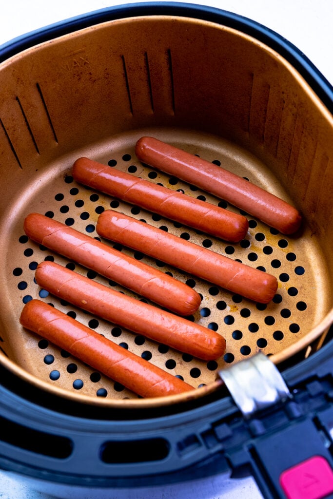 Hot dogs uncooked in the basket of an air fryer.