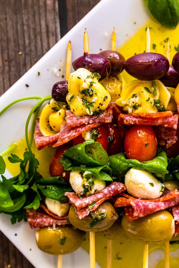 Antipasto Skewers served on a white plate drizzled with homemade dressing.