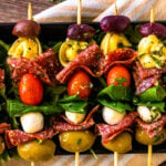 Antipasto skewers with olives and pasta lined up on a serving platter.