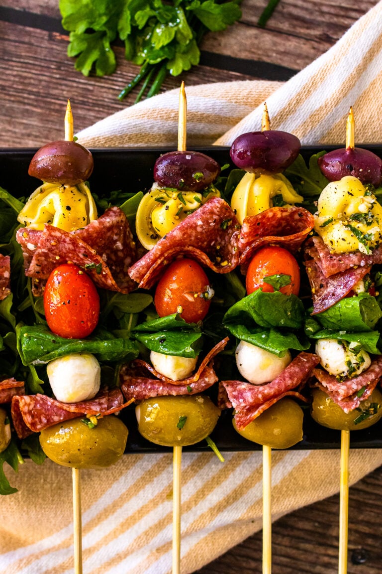 Antipasto skewers with olives and pasta lined up on a serving platter.