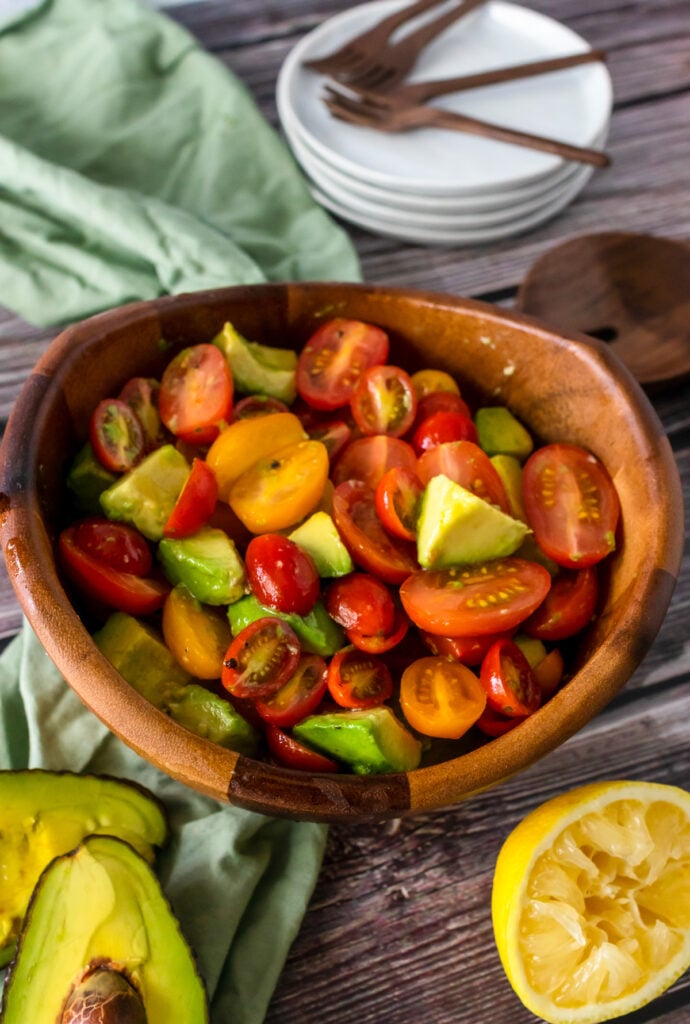 Avocado Tomato Salad in a wooden bowl ready to serve on white plates.