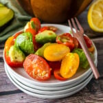4 white plates stacked with Avocado Tomato Salad and a wooden fork.