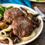 2 hamburger steak patties served with cooked onions and mushrooms and green beans on a plate.