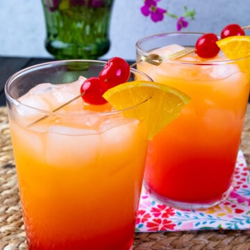 2 pretty glasses of Tequila Sunrise cocktails on placemants with napkins.