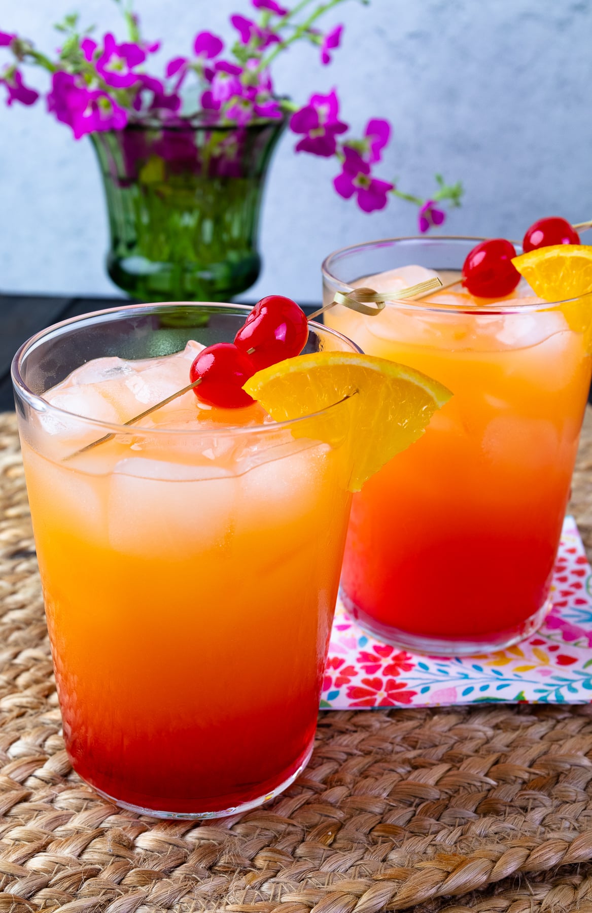 2 pretty glasses of Tequila Sunrise cocktails on placemants with napkins.