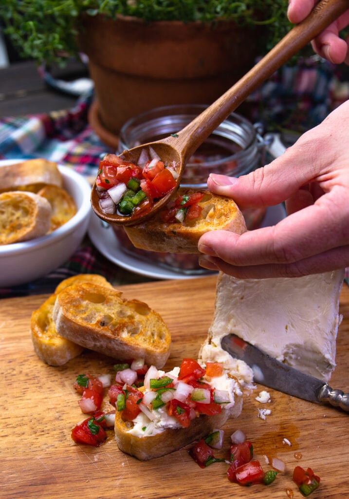 Hand holding toast and spoon with tomato relish for appetizers.