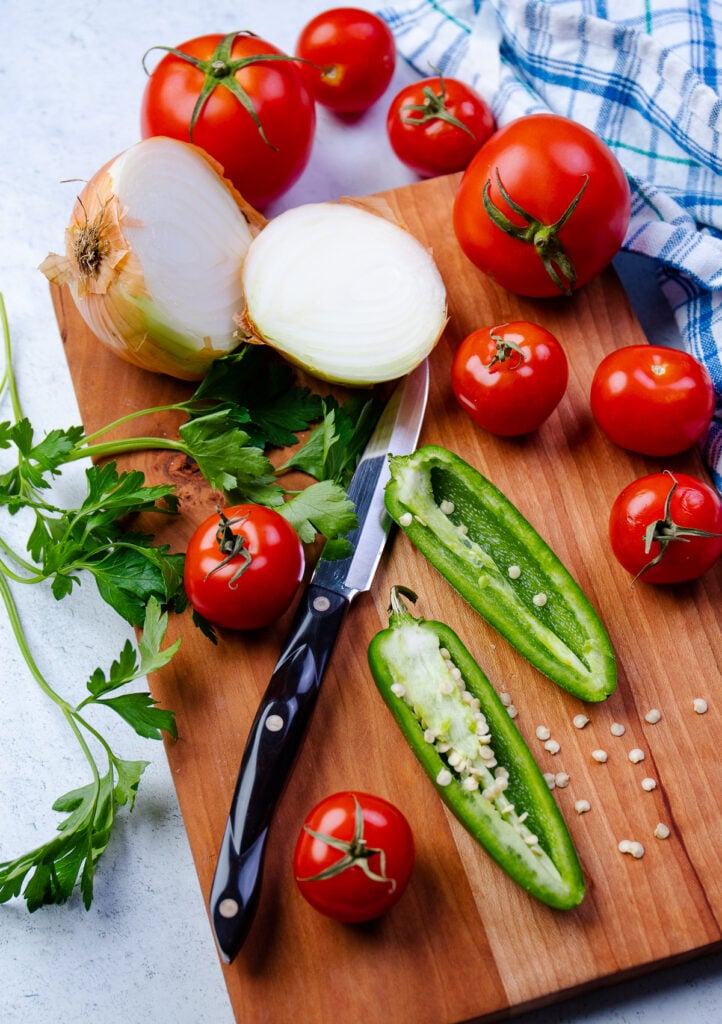 Tomatos, onion, jalapeno and parsley on a cutting board with a knife.