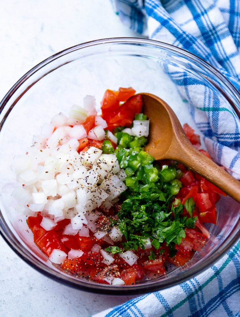Onion, tomato, peppers and a wooden spoon in a bowl for tomato relish.