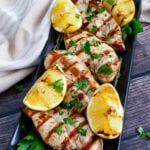 Grilled lemon chicken hero served on black rectangular plate with lemon slices and fresh parsley garnish