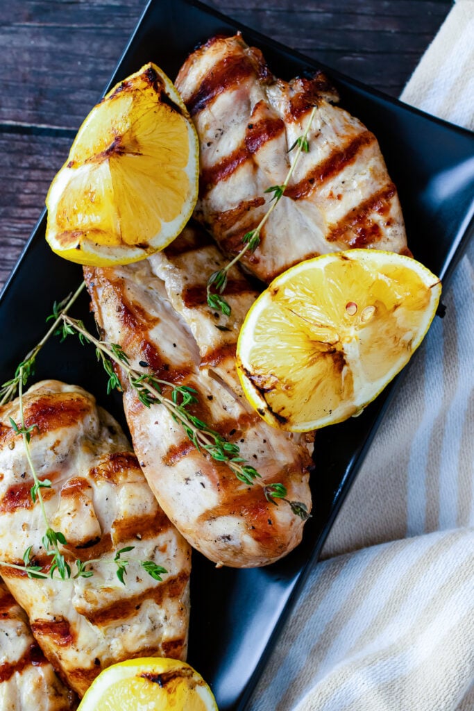 Grilled lemon chicken platter with charred lemon halves and fresh thyme sprigs on black rectangular plate