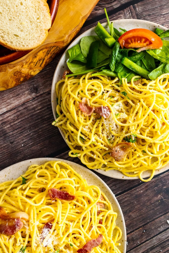 Two plates of Pasta Carbonara served with spinach and tomatoes.