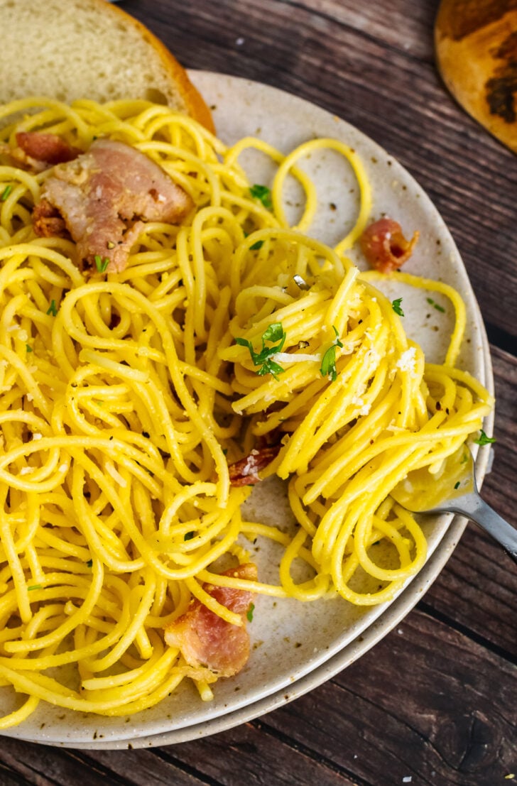 Pasta Carbonara on a plate twirled with a fork served with bread.