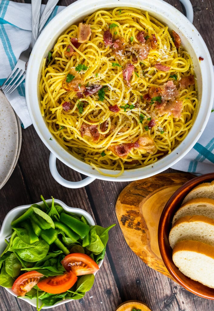 Pasta Carbonara in a white pot served with a salad and bread.