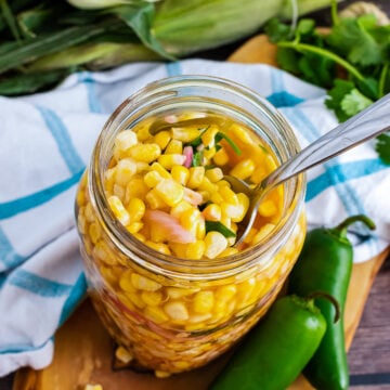 Pickled Corn with red onions and jalapenos in a jar served with a spoon.